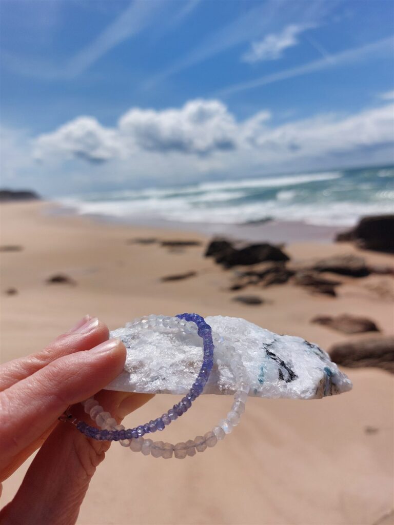 Bransoletki z tanzanitu i kamienia księżycowego przy białym krysztale na plaży